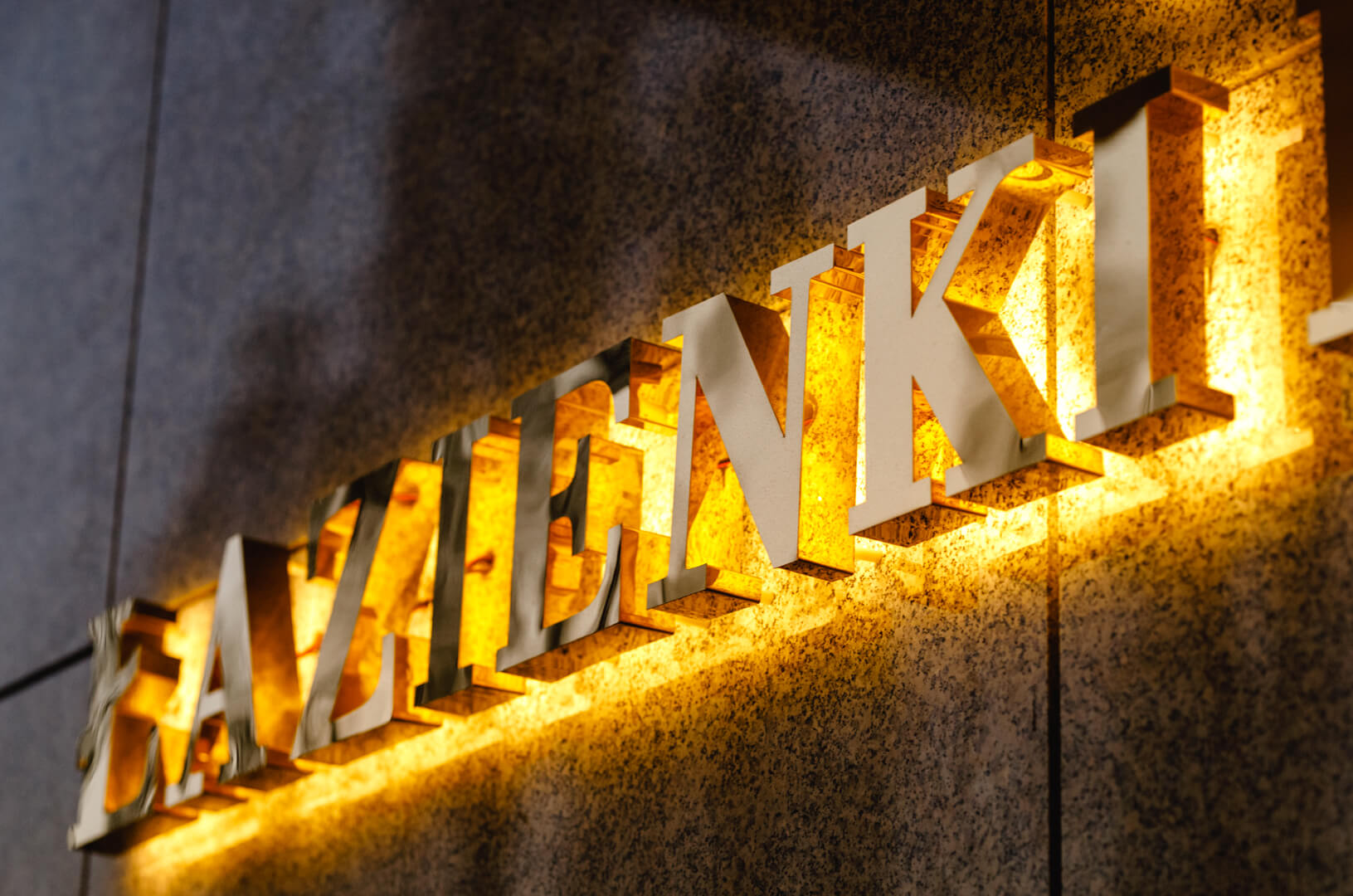 Bad Residenz-Schriftzug aus Edelstahl in Gold, LED-Hintergrundbeleuchtung an der Wand, mit einer Krone im Logo.